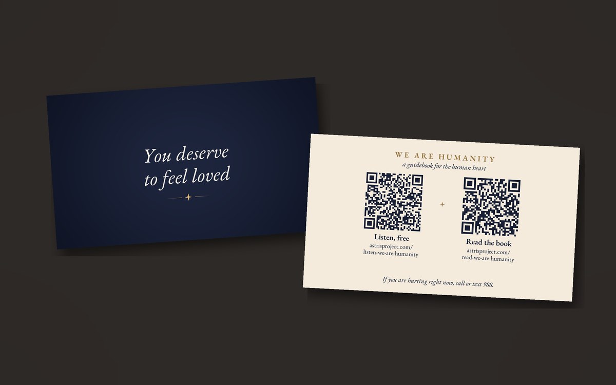 The two sides of the card: on deep night blue, &ldquo;You deserve to feel loved&rdquo; in cream italic above a small gold star; on cream, We Are Humanity, two QR codes marked Listen, free and Read the book, and a line about 988.
